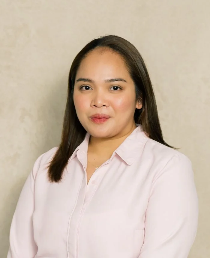 Portrait of a woman with long dark hair wearing a light pink blouse against a beige background.