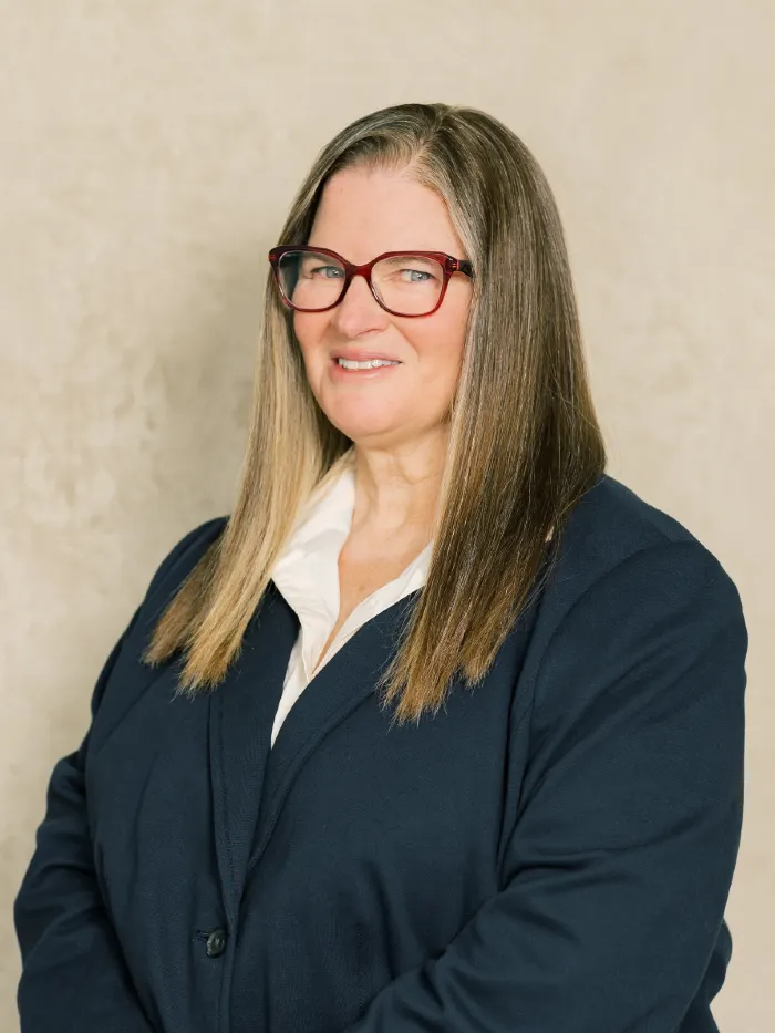 Professional portrait of a woman with long hair, red glasses, white blouse, and navy blazer.