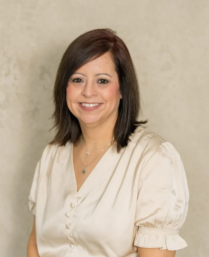Professional portrait of a smiling woman with dark hair wearing a cream blouse against a neutral background.
