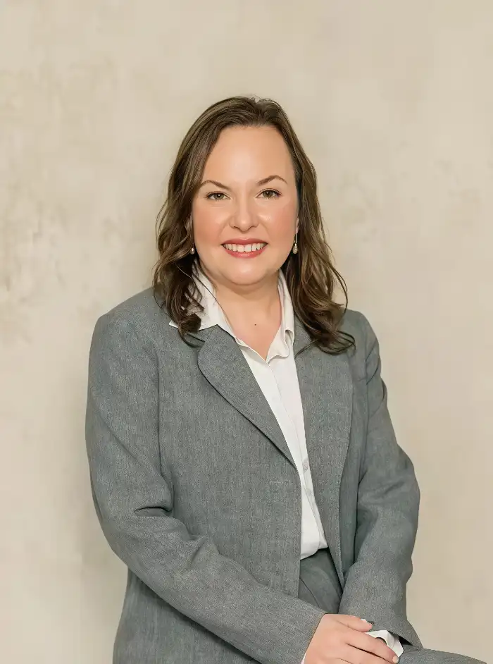 Professional portrait of a smiling woman wearing a gray suit and white blouse against a beige background.