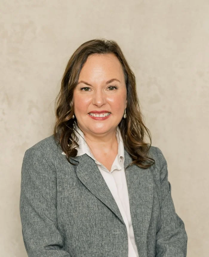 Professional portrait of a woman with brown hair wearing a gray blazer and white blouse.
