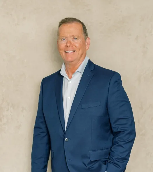 Professional portrait of a middle-aged man in a blue suit and white shirt, smiling against a beige background.