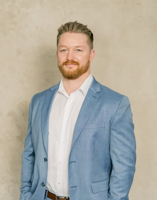 Professional portrait of a man with light brown hair and beard wearing a light blue suit and white shirt.