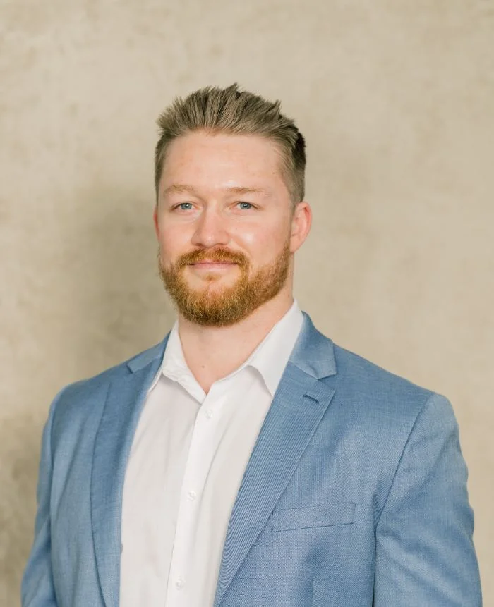 Professional portrait of a man with red beard wearing blue blazer and white shirt.
