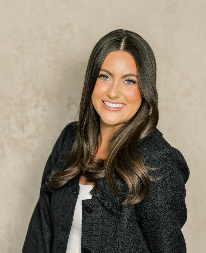 Professional portrait of a smiling woman with long dark hair wearing a black jacket.