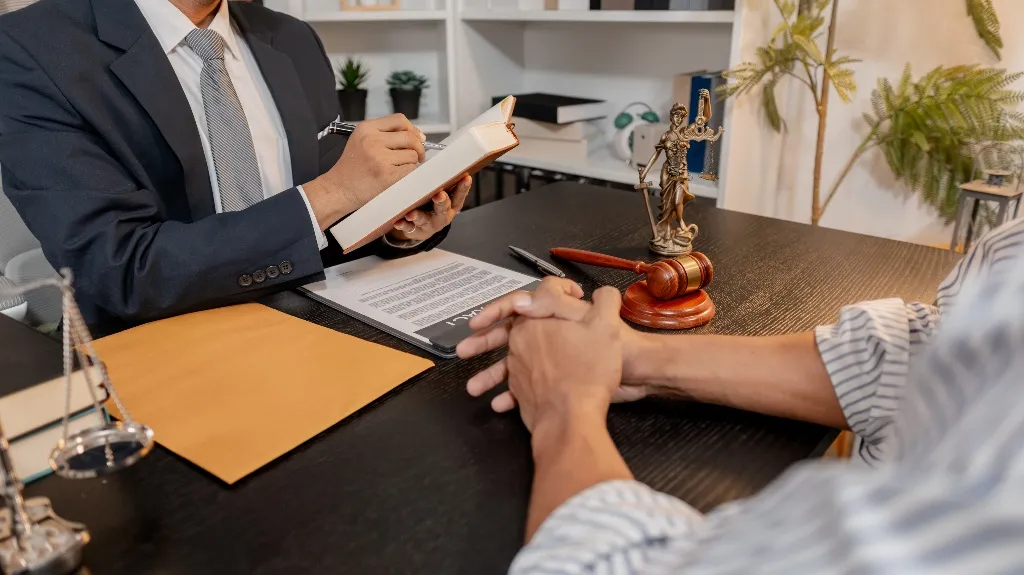 Two individuals at a desk, one in a suit writing in a book, with legal symbols and documents present.