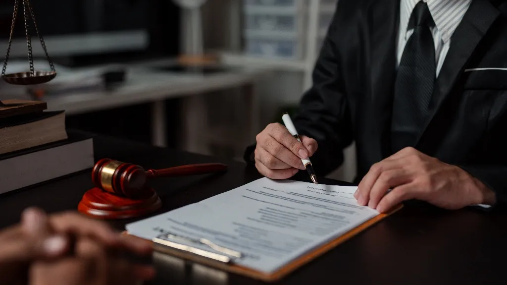 Legal professional in suit reviewing and signing documents at desk with gavel and scales.