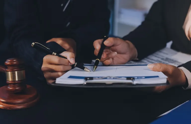 Two individuals in business attire reviewing and signing documents near a wooden gavel.