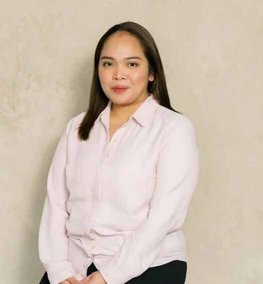 Professional portrait of a woman with long dark hair wearing a light pink blouse against a beige background.