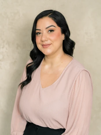Portrait of a woman with long black hair wearing a light pink blouse against a neutral background.