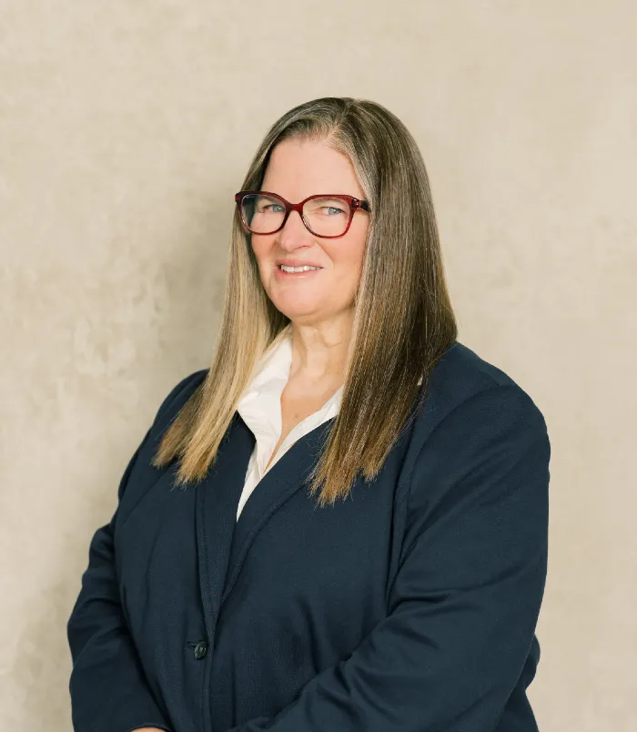 Professional portrait of a woman with long straight hair, wearing red glasses and a dark blazer.