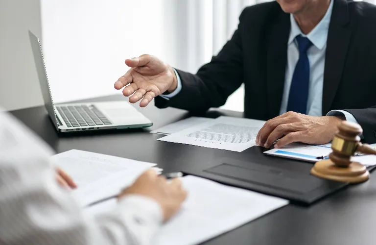 Two professionals in a meeting with documents, laptop, and a wooden gavel on the table.