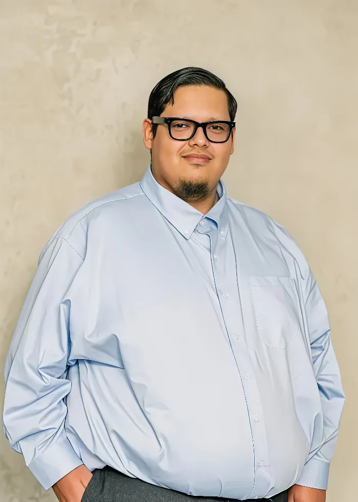 Portrait of a man wearing black glasses and a light blue button-up shirt against a beige background.