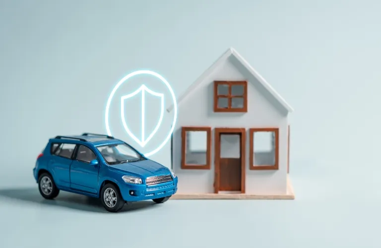 Blue toy car and small white model house with illuminated shield icon on light background.